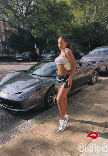 Joyce, slim brunette escort in London wearing a mini skirt and sneakers outside next to a Ferrari