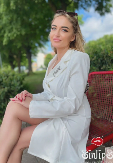 Zircona, Estonian blonde escort in white coat sitting on a bench outside